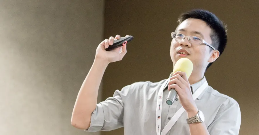 文章主視覺。演講中的陳冠廷醫師，一手持簡報筆，一手握著麥克風。